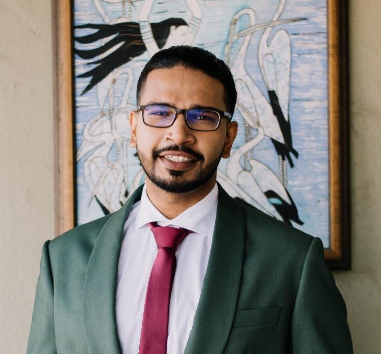 Marques Jeevan Menon, in a dark green blazer, a white shirt and a red tie